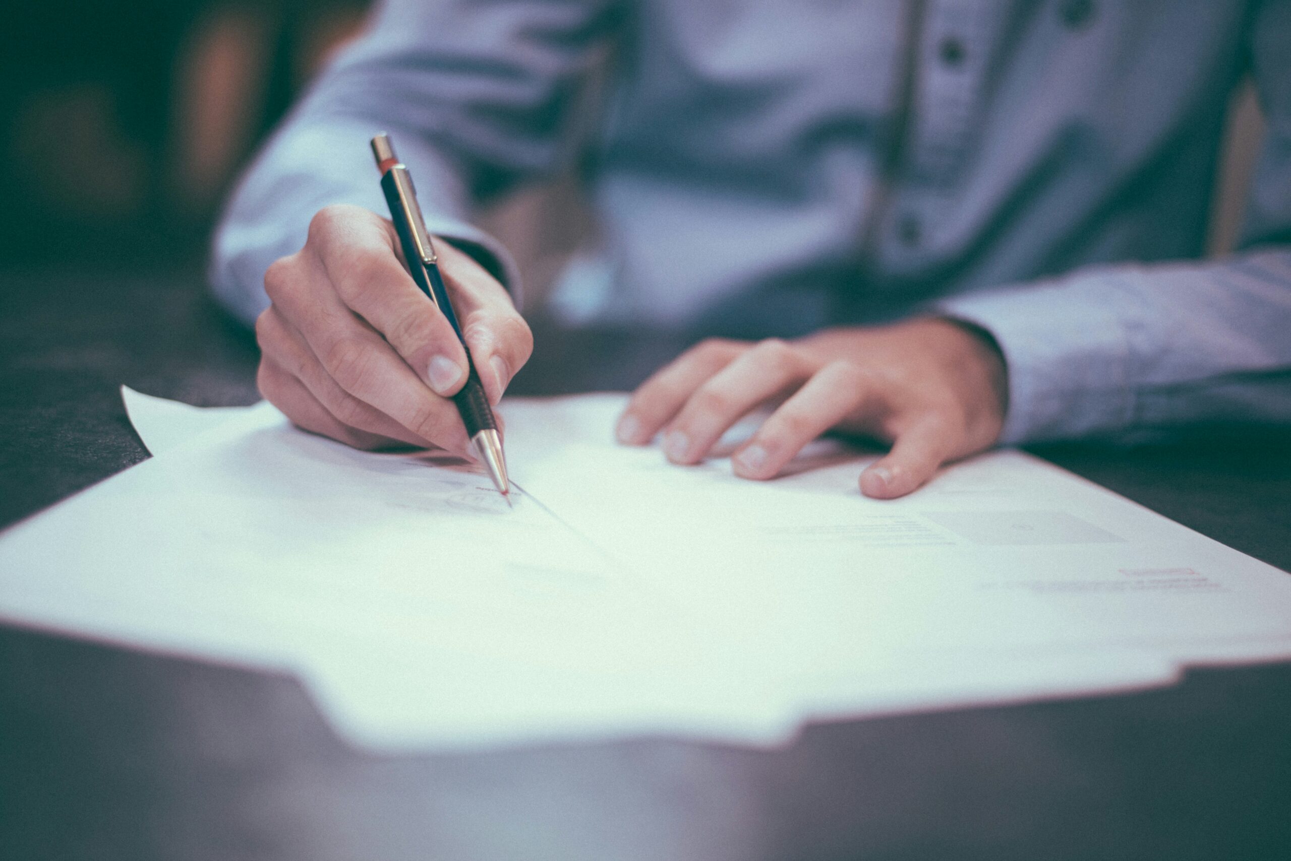 Hands signing a purchase agreement, the closing step in buying an equipment dealership